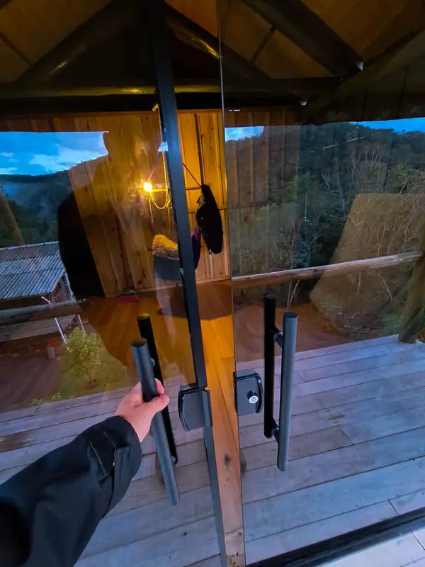 Puxador de porta de correr em vidro com perfil preto, em varanda de madeira ao entardecer