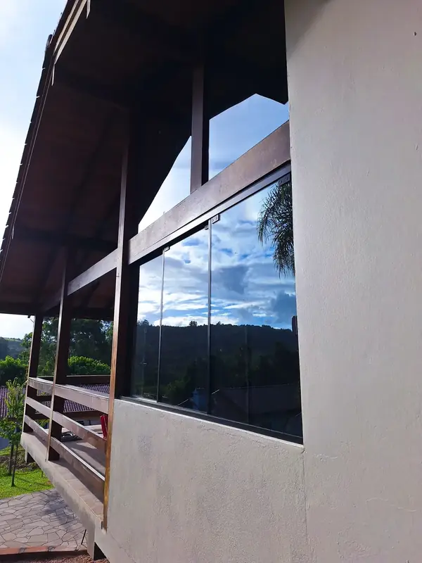 Janela de alumínio preto sob varanda de madeira, com reflexo do céu