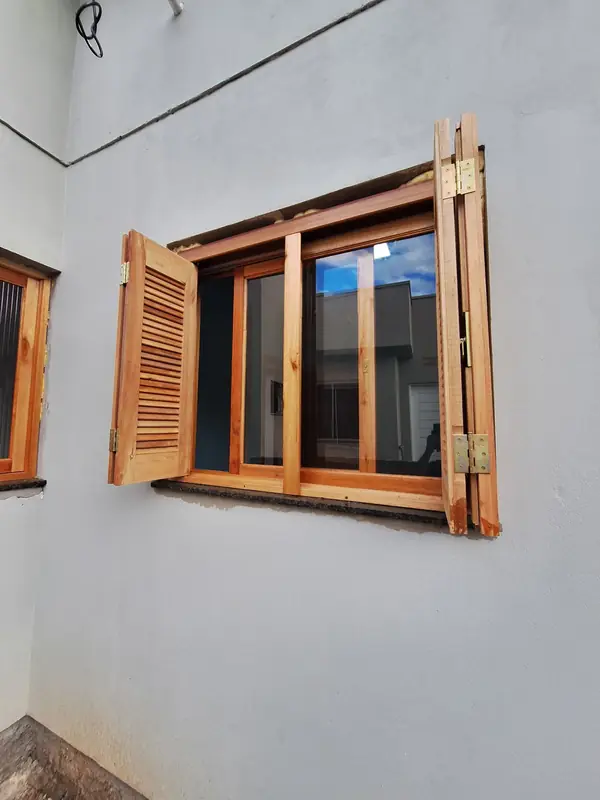 Janela de madeira com vidro e venezianas em fachada branca