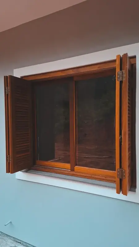 Janela de madeira com venezianas abertas em parede clara