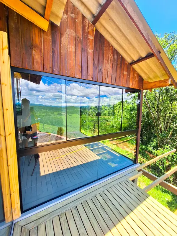 Varanda envidraçada de cabana de madeira, com vista para o vale