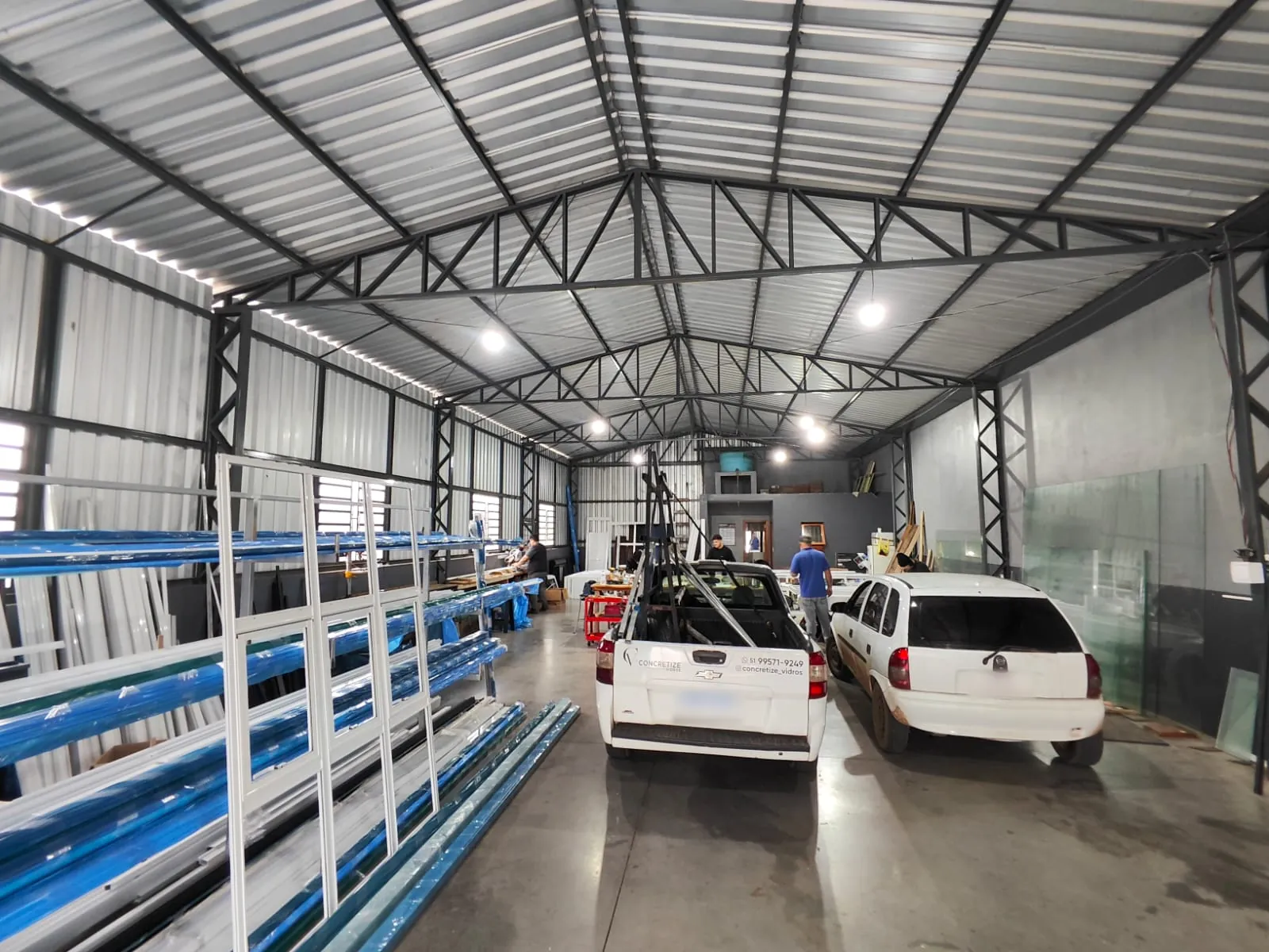 Interior do pavilhão em Taquara–RS, com estrutura metálica, racks de perfis de alumínio e área de produção