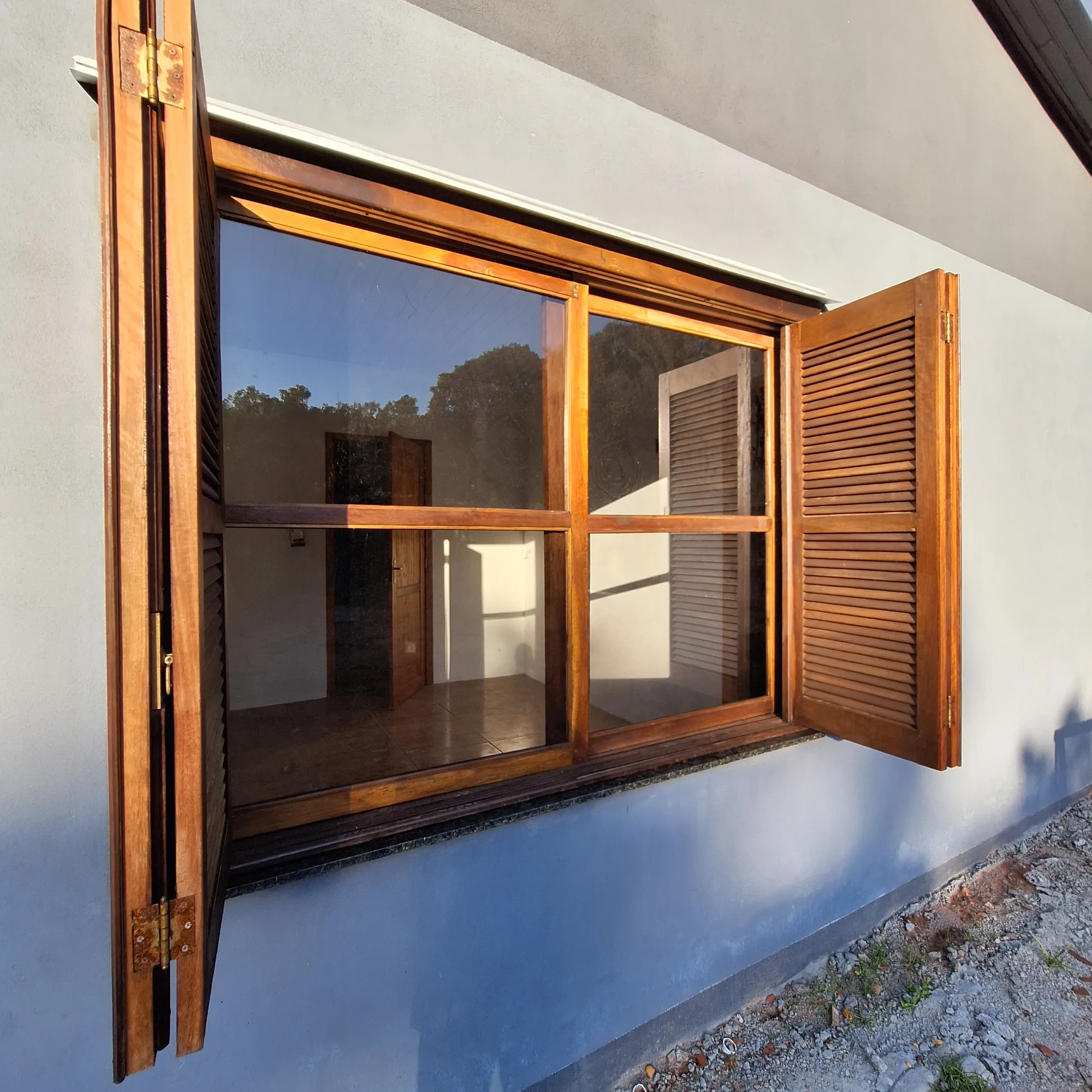 Janela de madeira com vidro instalado, venezianas abertas, em fachada azul