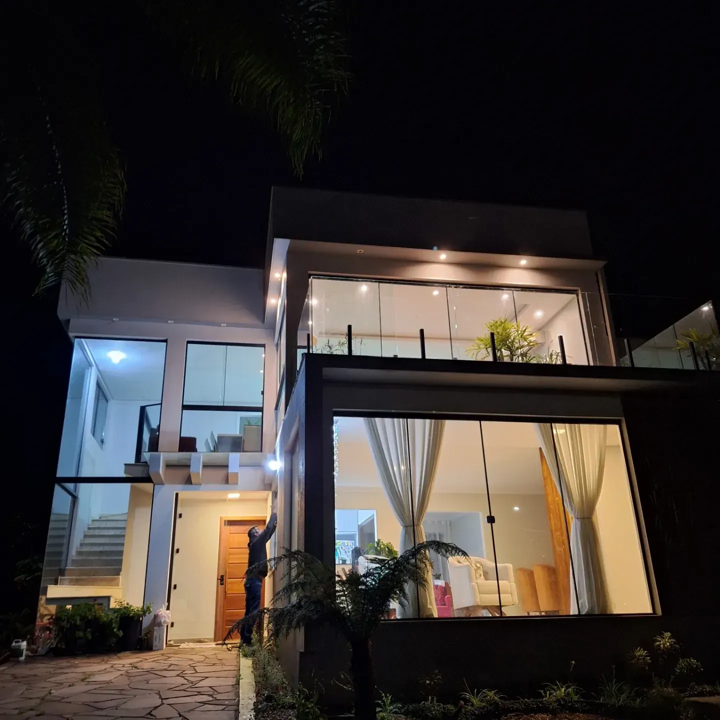 Casa moderna à noite, com panos de vidro iluminados e guarda-corpo de vidro no terraço